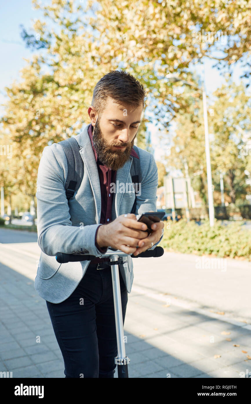 Businessman checking cell phone on scooter Stock Photo