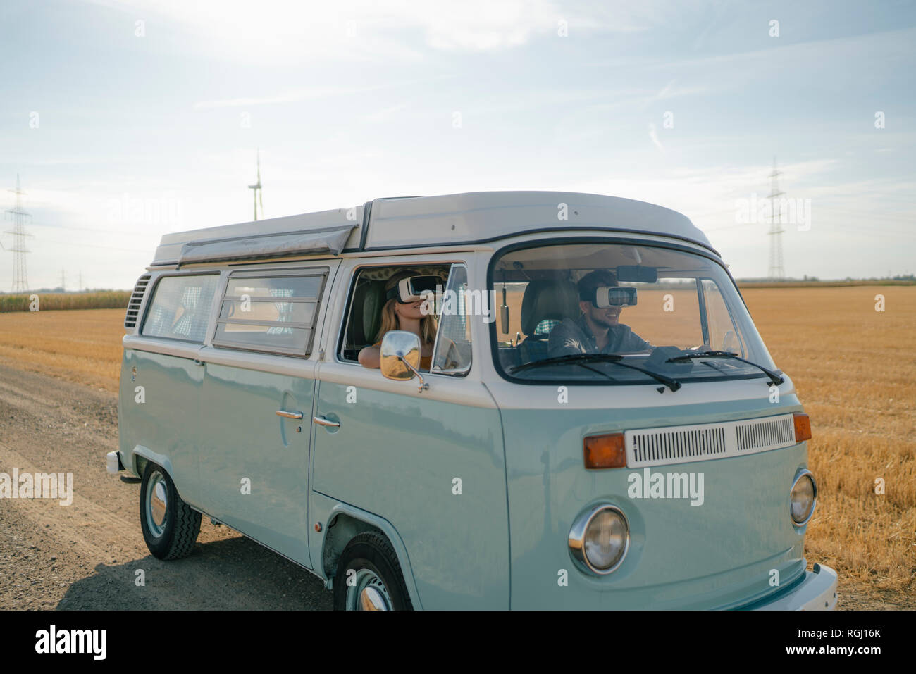 Young couple wearing VR glasses driving camper van in rural landscape Stock Photo