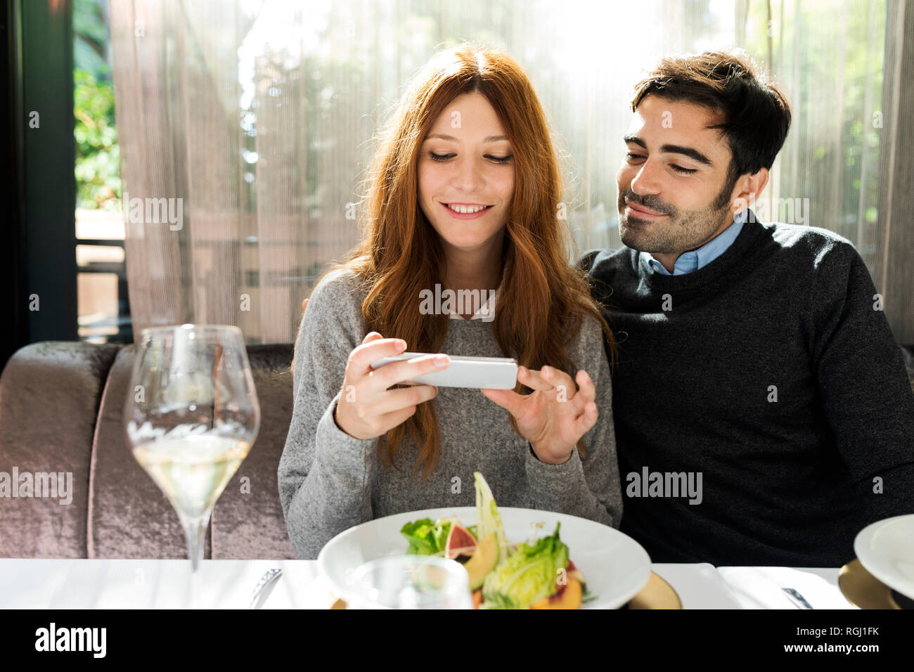Smiling couple using cell phone in a restaurant Stock Photo