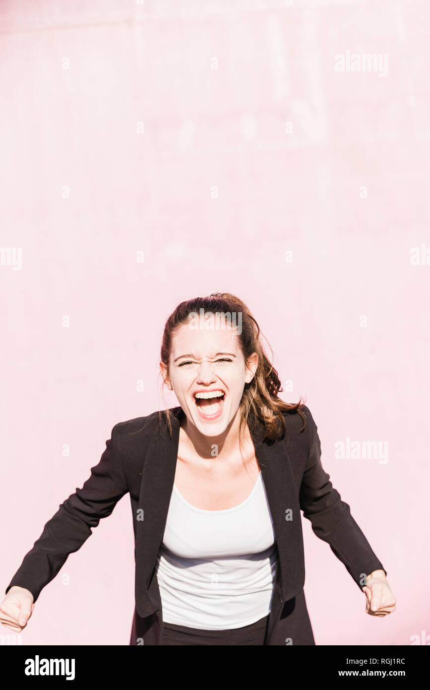 Portrait of screaming young woman in front of pink wall Stock Photo