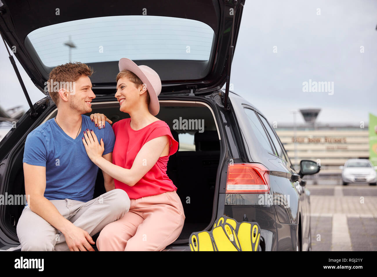 Happy young couple sitting in car boot at the airport Stock Photo