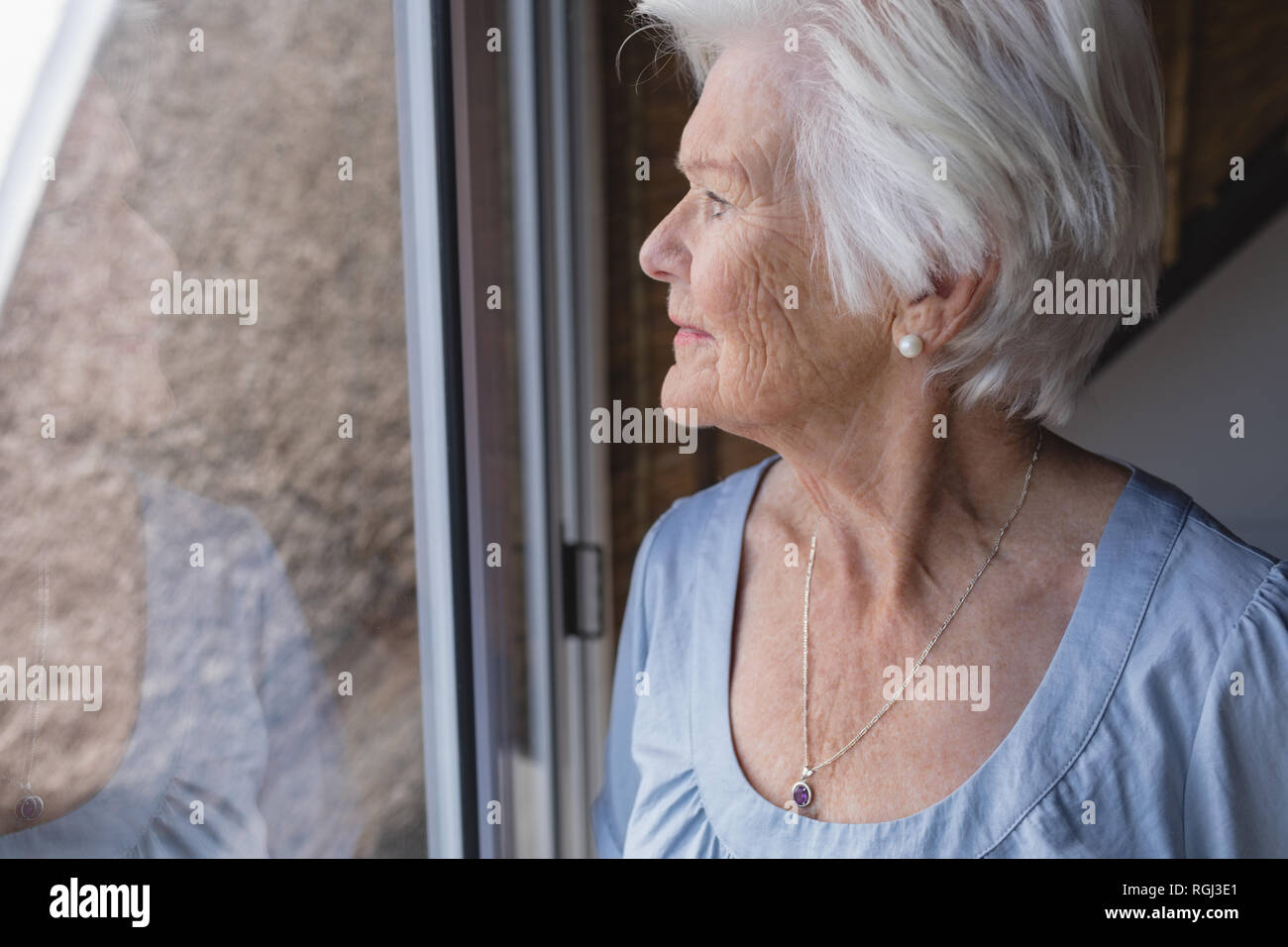 Senior woman looking through window Stock Photo - Alamy