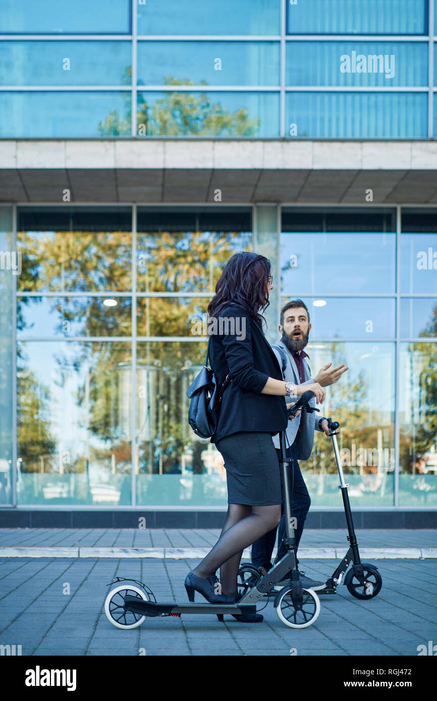 Businessman and businesswoman with scooters talking on pavement Stock Photo