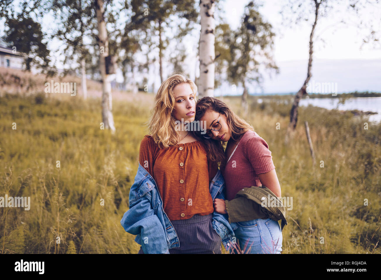 Two girl friends leaning on each other on a lakeshore Stock Photo