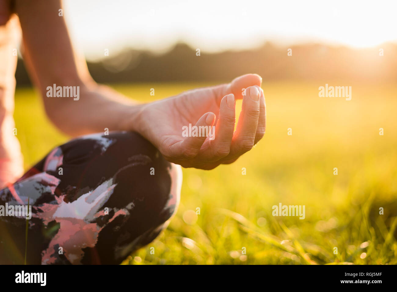 Detail of woman in lotus position on rural meadow at sunset Stock Photo