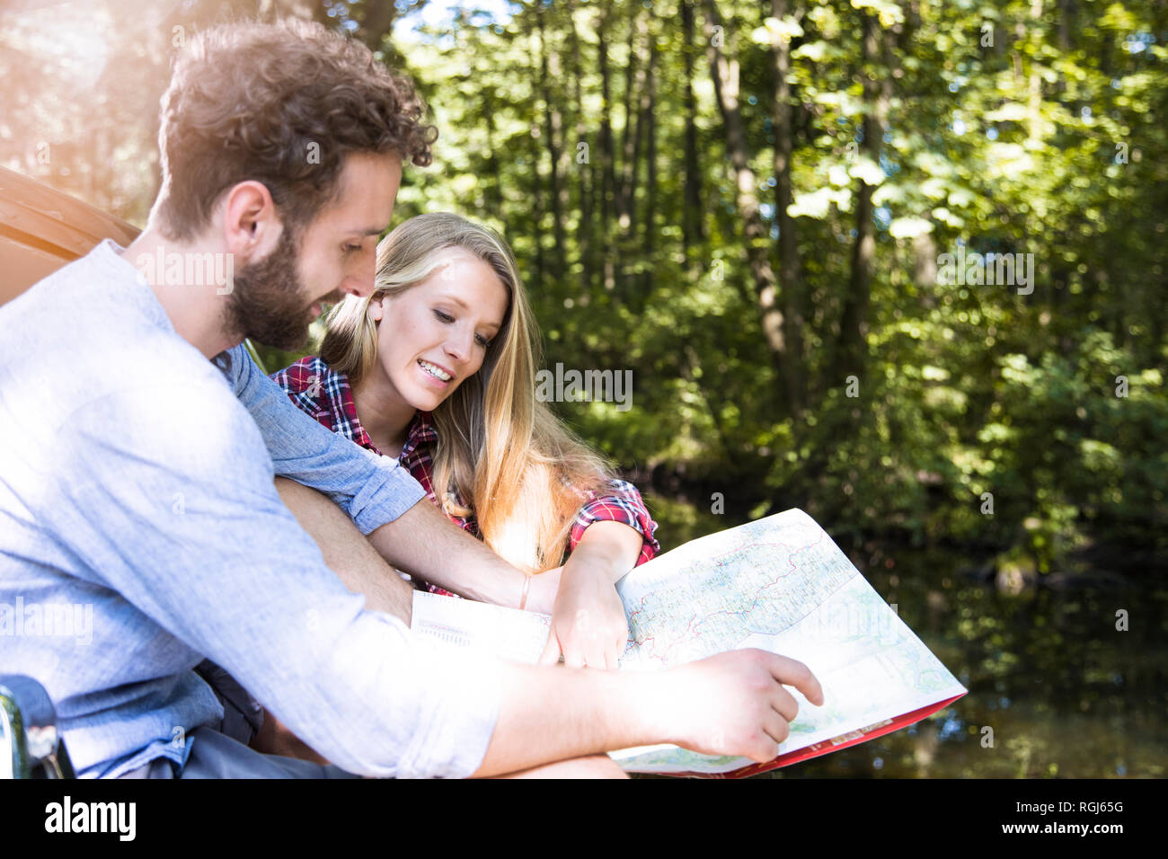 Smiling young couple reading map at a brook Stock Photo