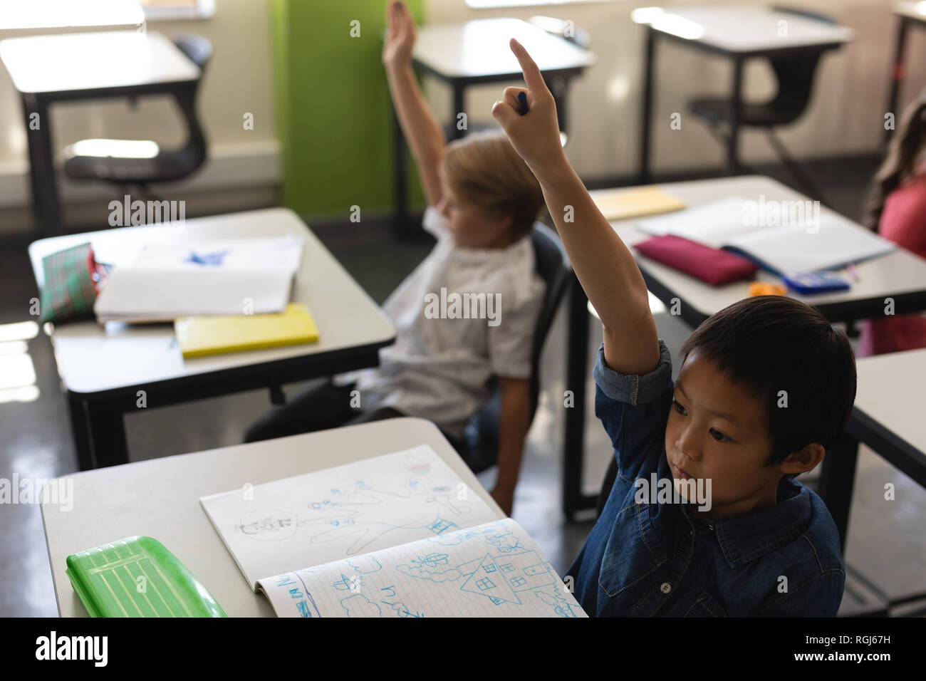Schoolboy raising hand in classroom Stock Photo