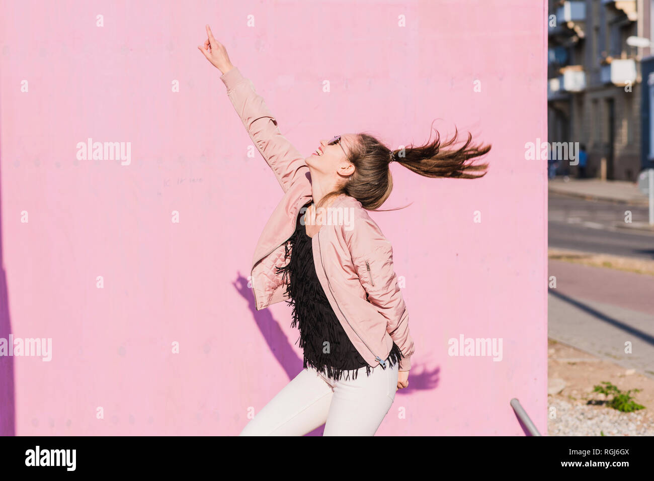 Happy young woman moving in front of pink wall Stock Photo - Alamy