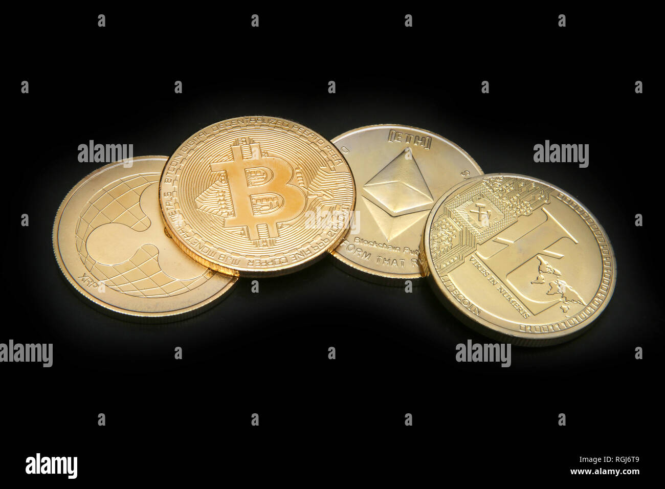 Litecoin, Ripple, Ethereum & Bitcoin gold coins representing cryptocurrenies against a black background. Stock Photo