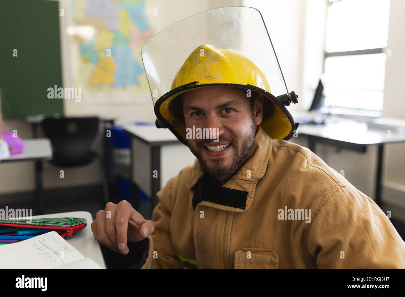 Front view of happy male firefighter with helmet in classroom Stock Photo