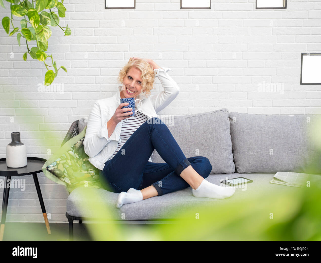 Portrait of smiling mature woman sitting on couch at home holding coffee mug Stock Photo