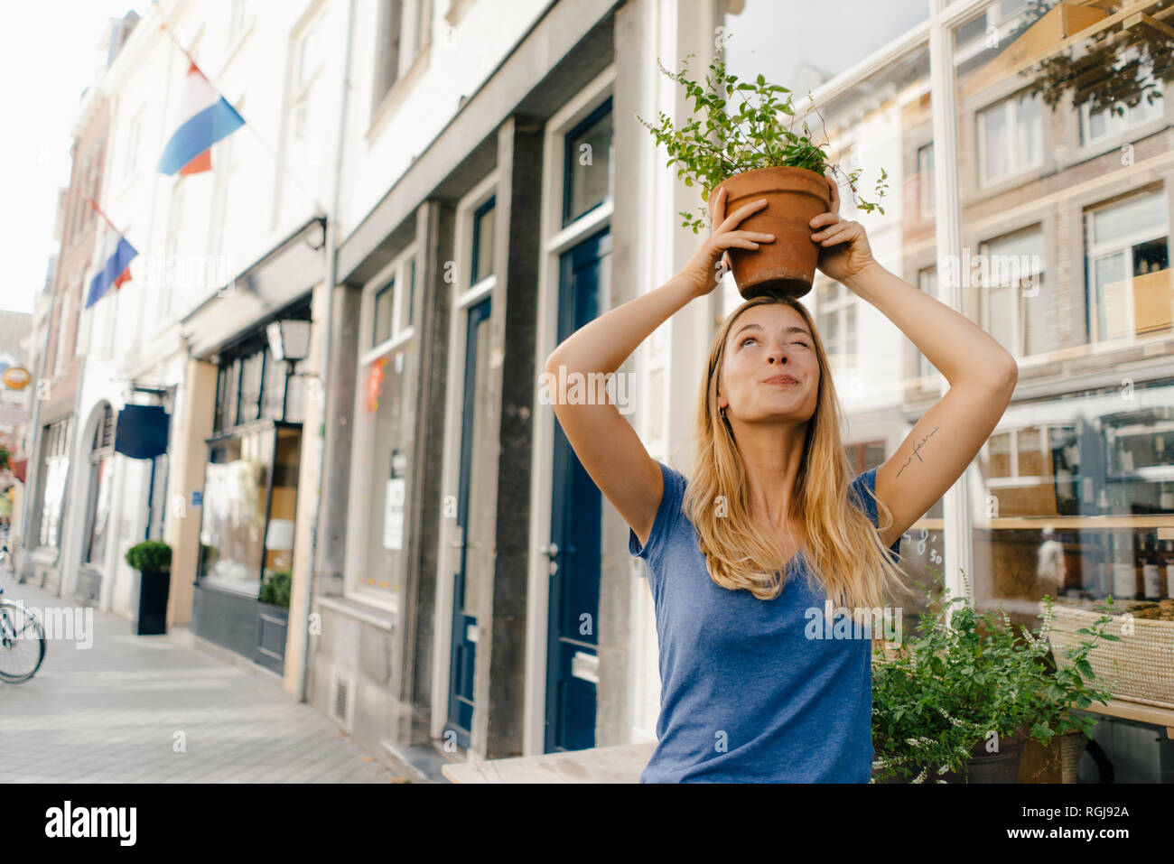 Netherlands, Maastricht, young woman balancing flowerpot on her head in the city Stock Photo