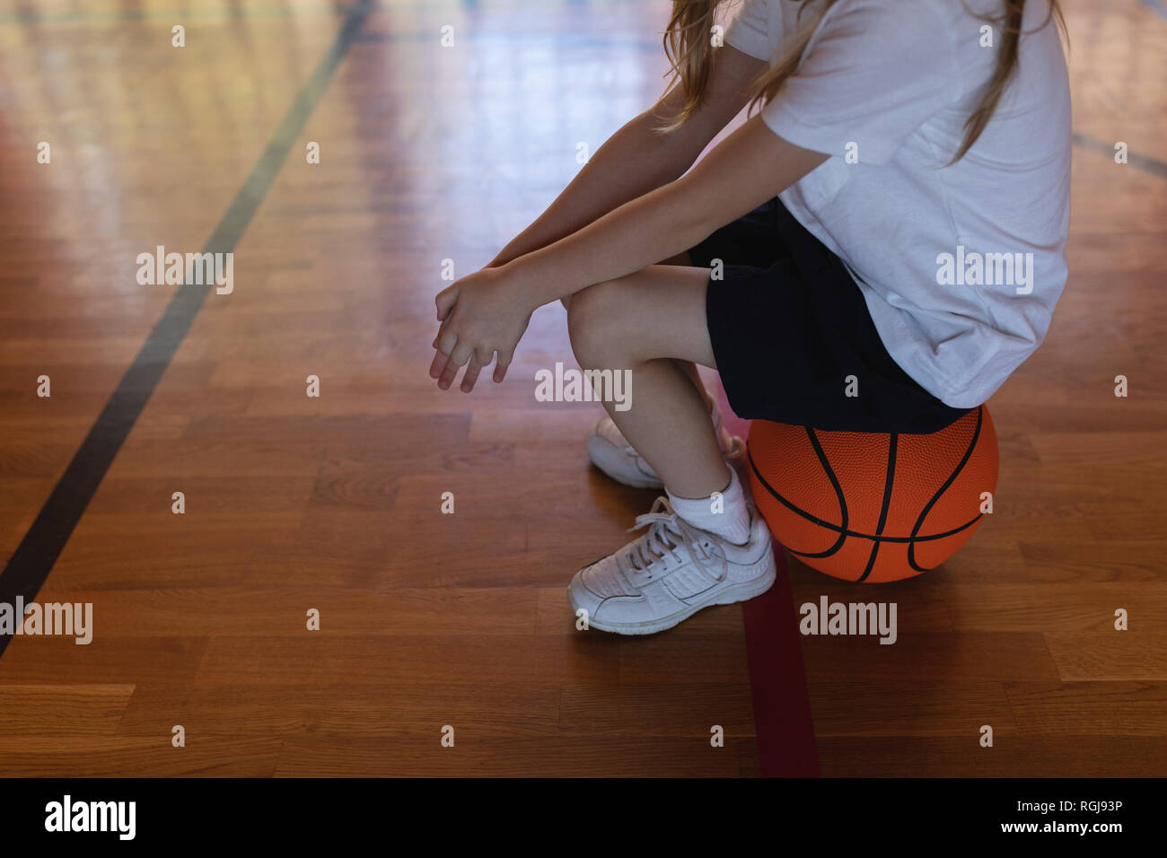 Low section of schoolgirl sitting on basketball at basketball court Stock Photo