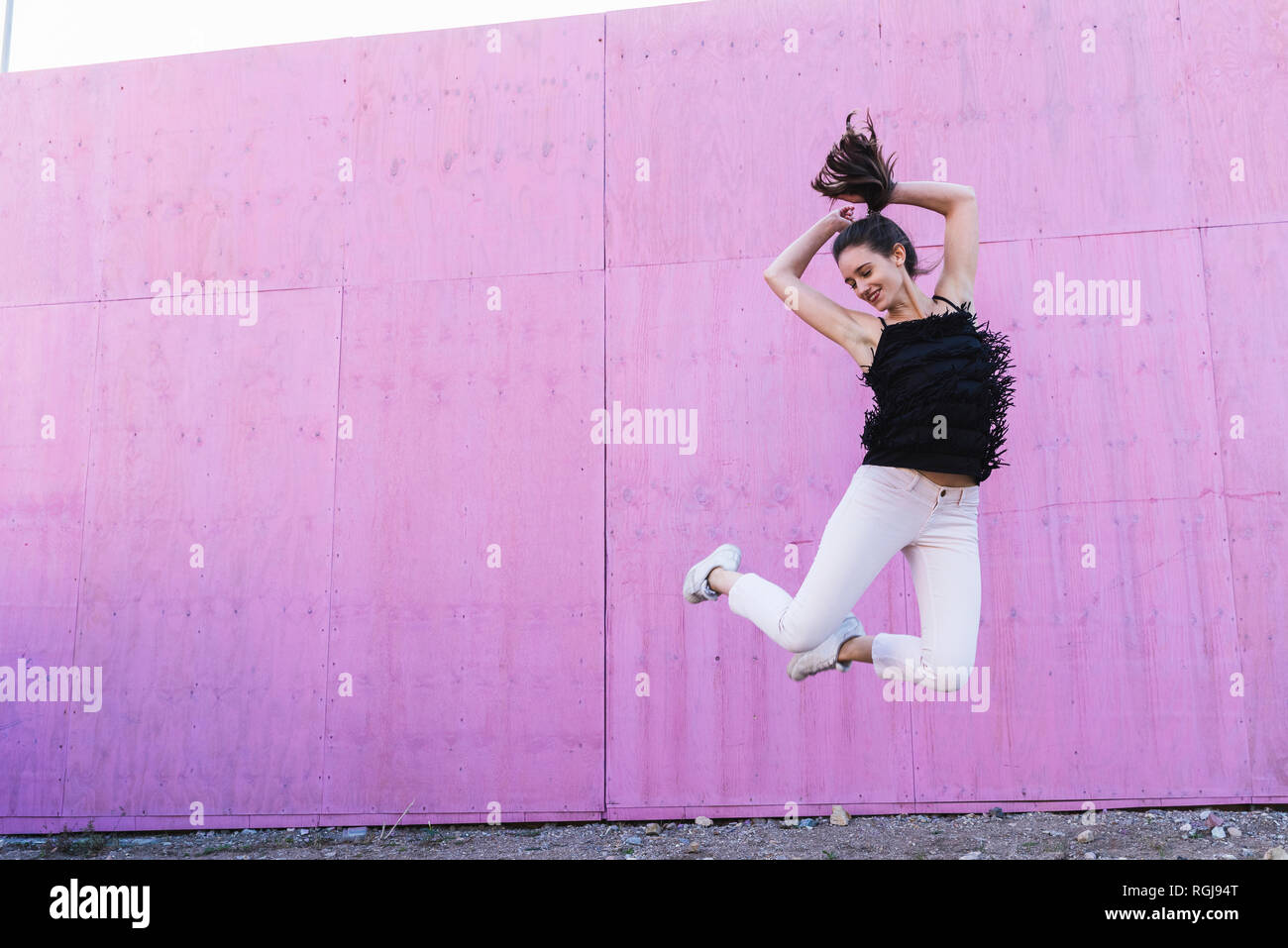 Exuberant young woman jumping in front of pink wall Stock Photo