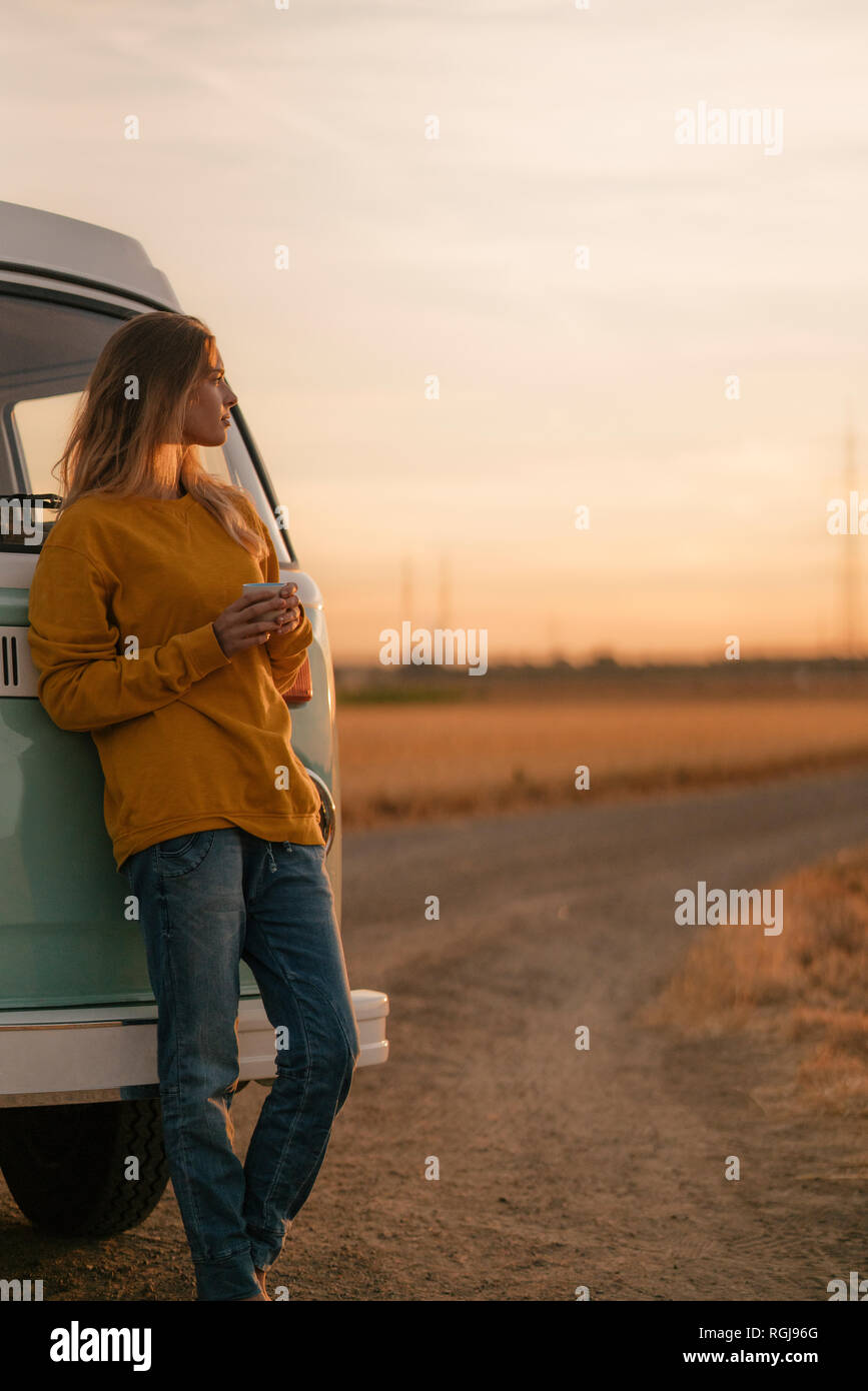 Young woman standing at camper van in rural landscape at sunset Stock Photo