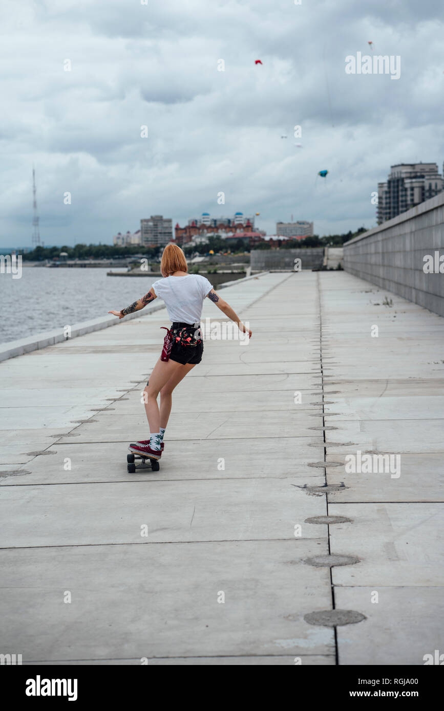 Rear view of young woman riding carver skateboard at the riverside Stock Photo