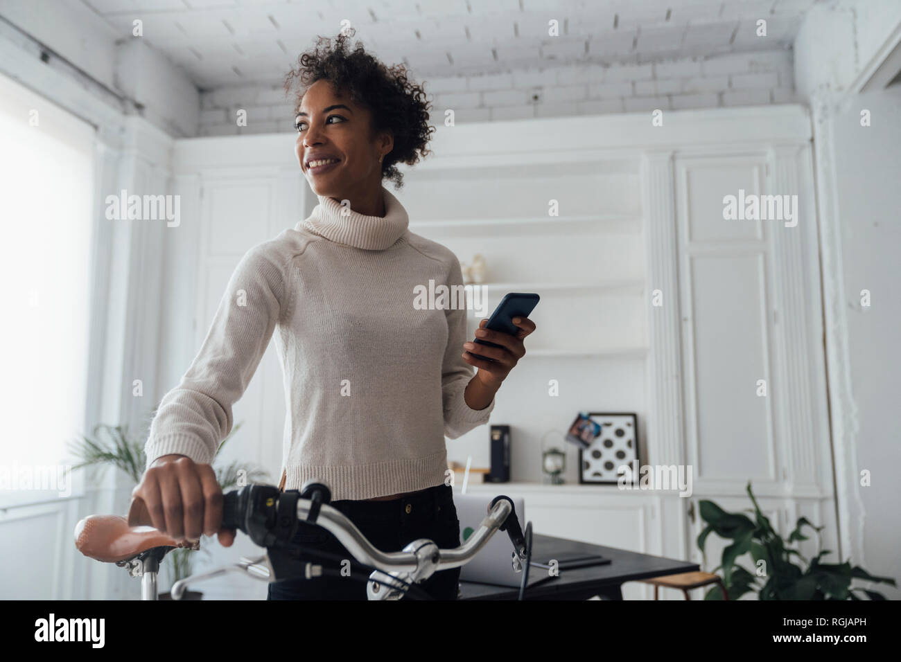 Mid adult woman leaving her home office, pushing bicycle, using smartphone Stock Photo
