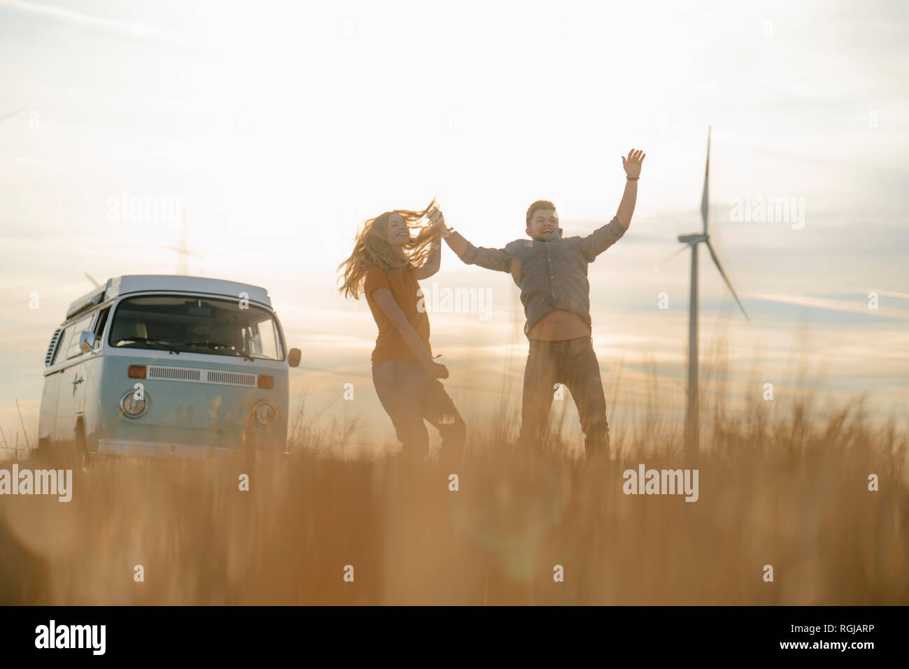 Exuberant couple at camper van in rural landscape with wind turbine in background Stock Photo