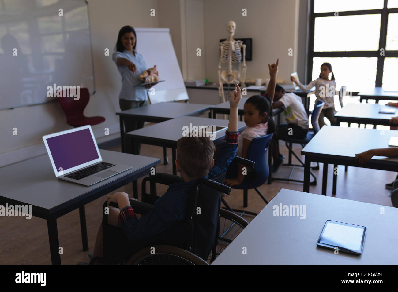 Front view of female teacher pointing his finger towards schoolkid in classroom of elementary school Stock Photo