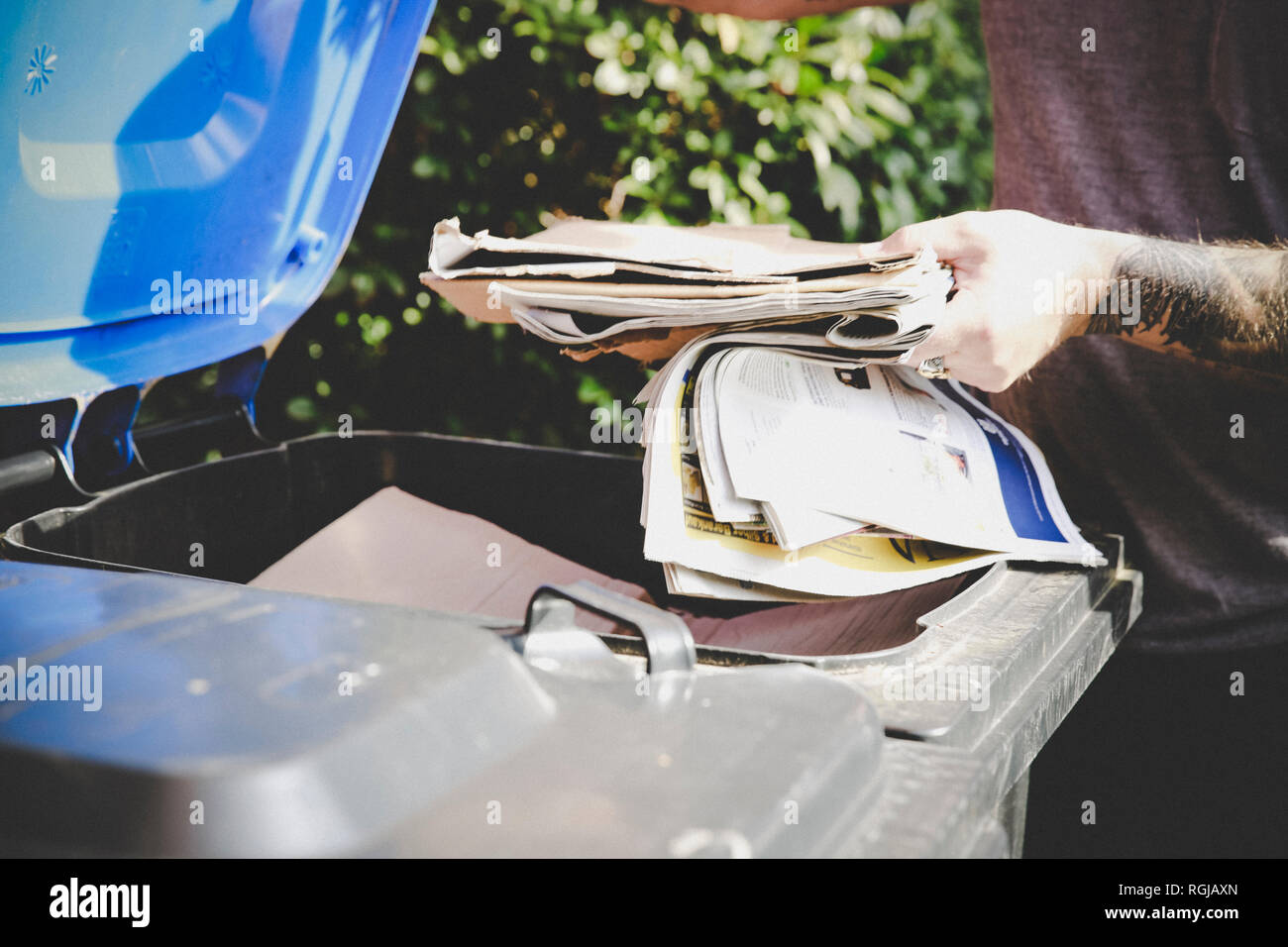 Tattooed man recycling waste paper in paper bank, partial view Stock Photo