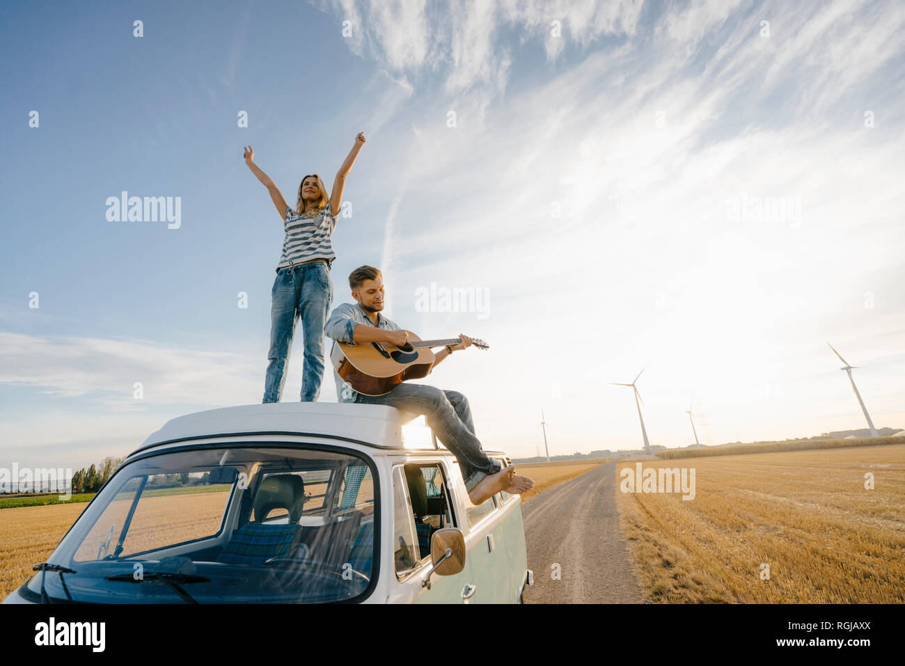 Happy couple with guitar on roof of a camper van in rural landscape ...