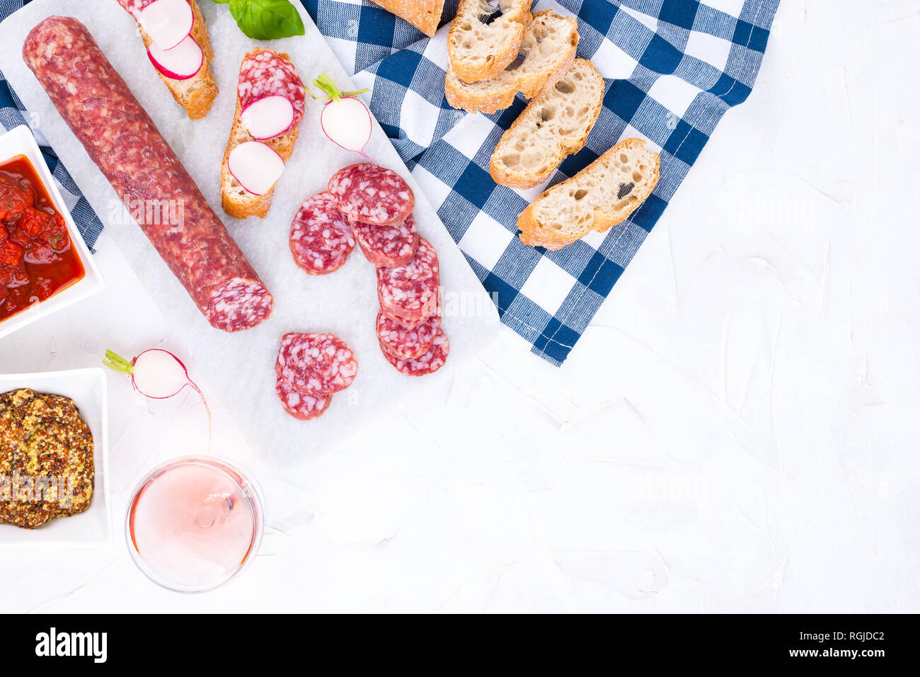 Italian salami on a white board and a stone background, a glass of rose