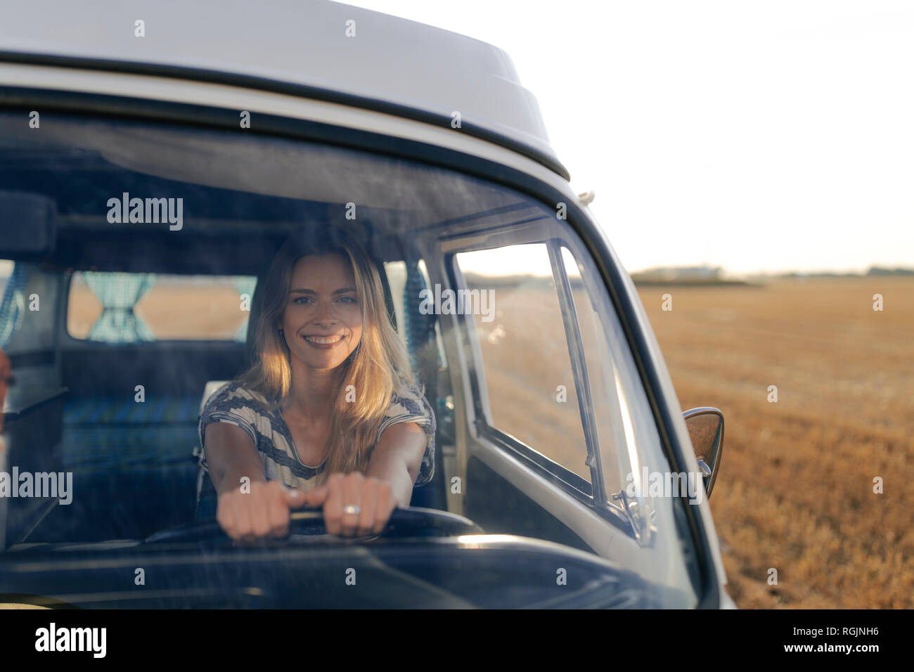Happy young woman driving camper van in rural landscape Stock Photo