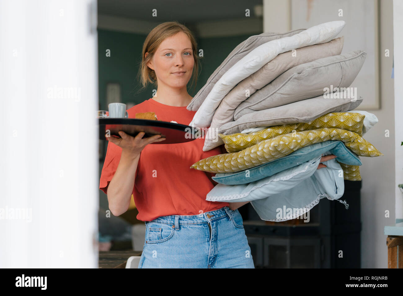 Portrait of young woman holding tray and cushions in a cafe Stock Photo
