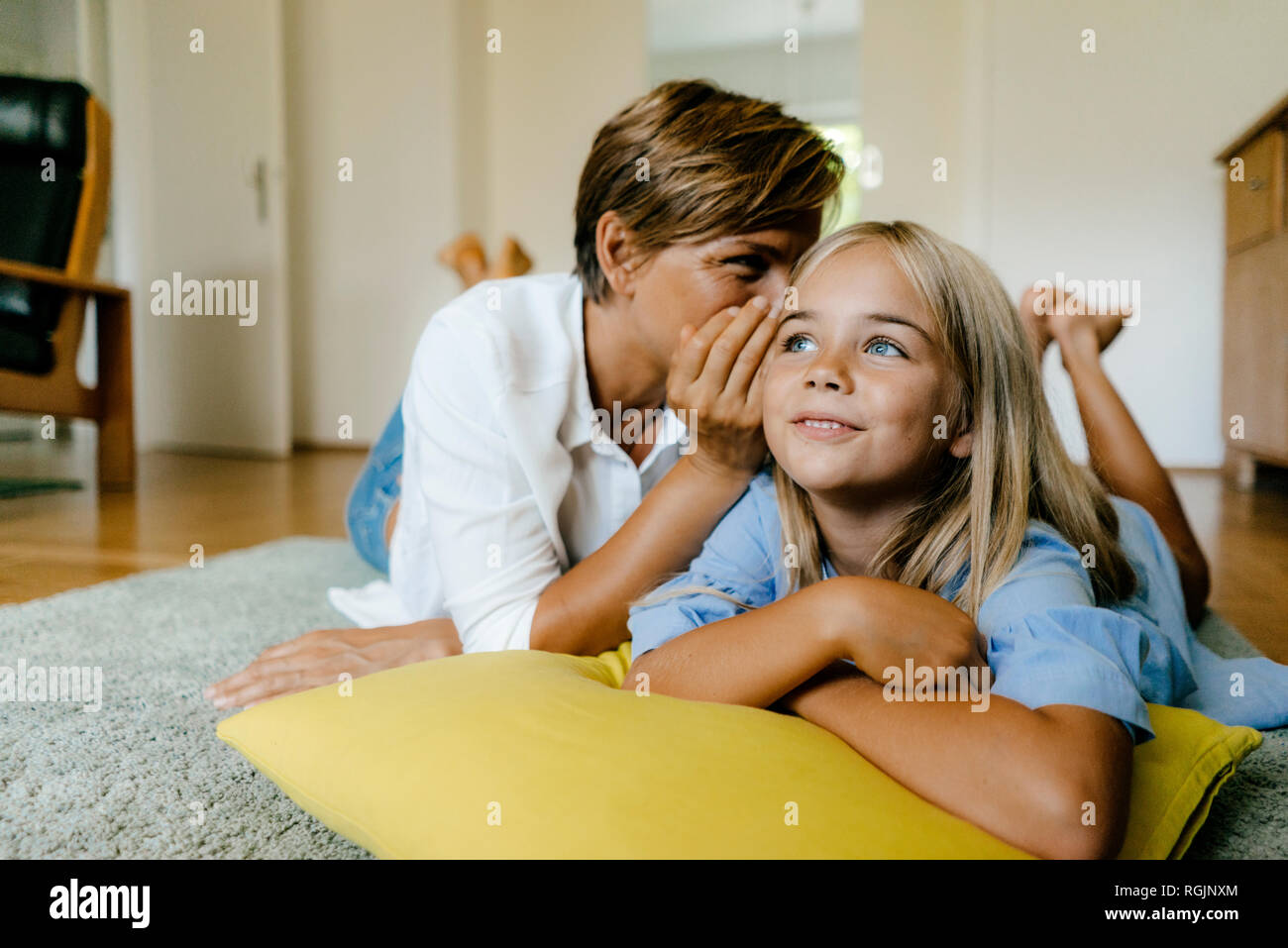 Mother and daughter lying on the floor at home whispering Stock Photo