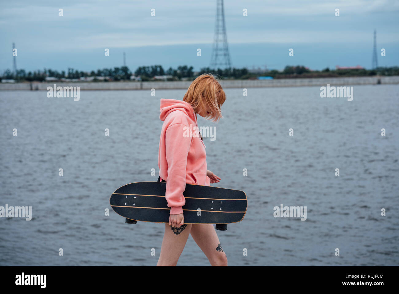 Young woman holding carver skateboard walking at the riverside Stock Photo