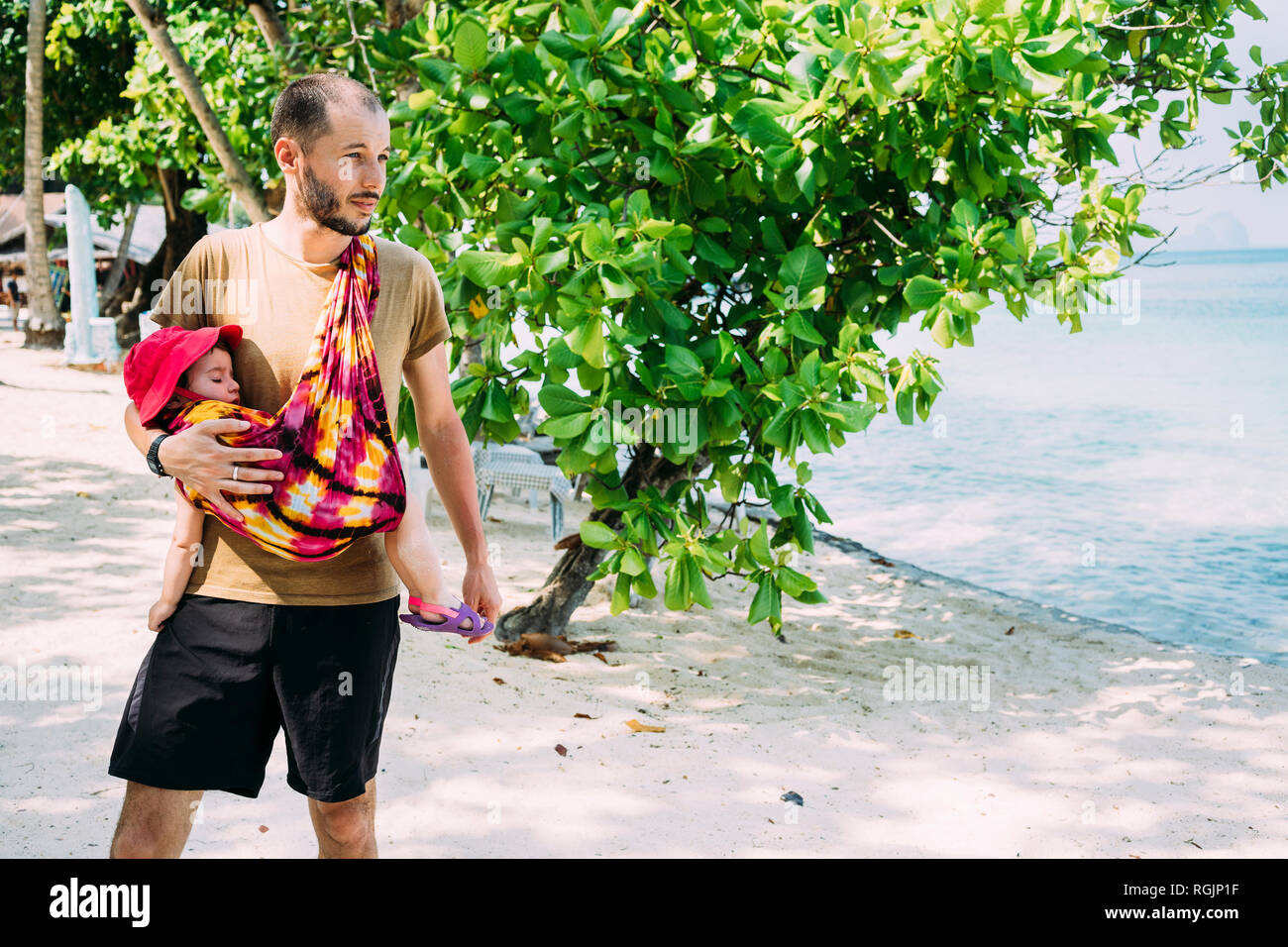 Thailand, Father with daughter, sleeping in baby sling at Khlong Chak Beach Stock Photo