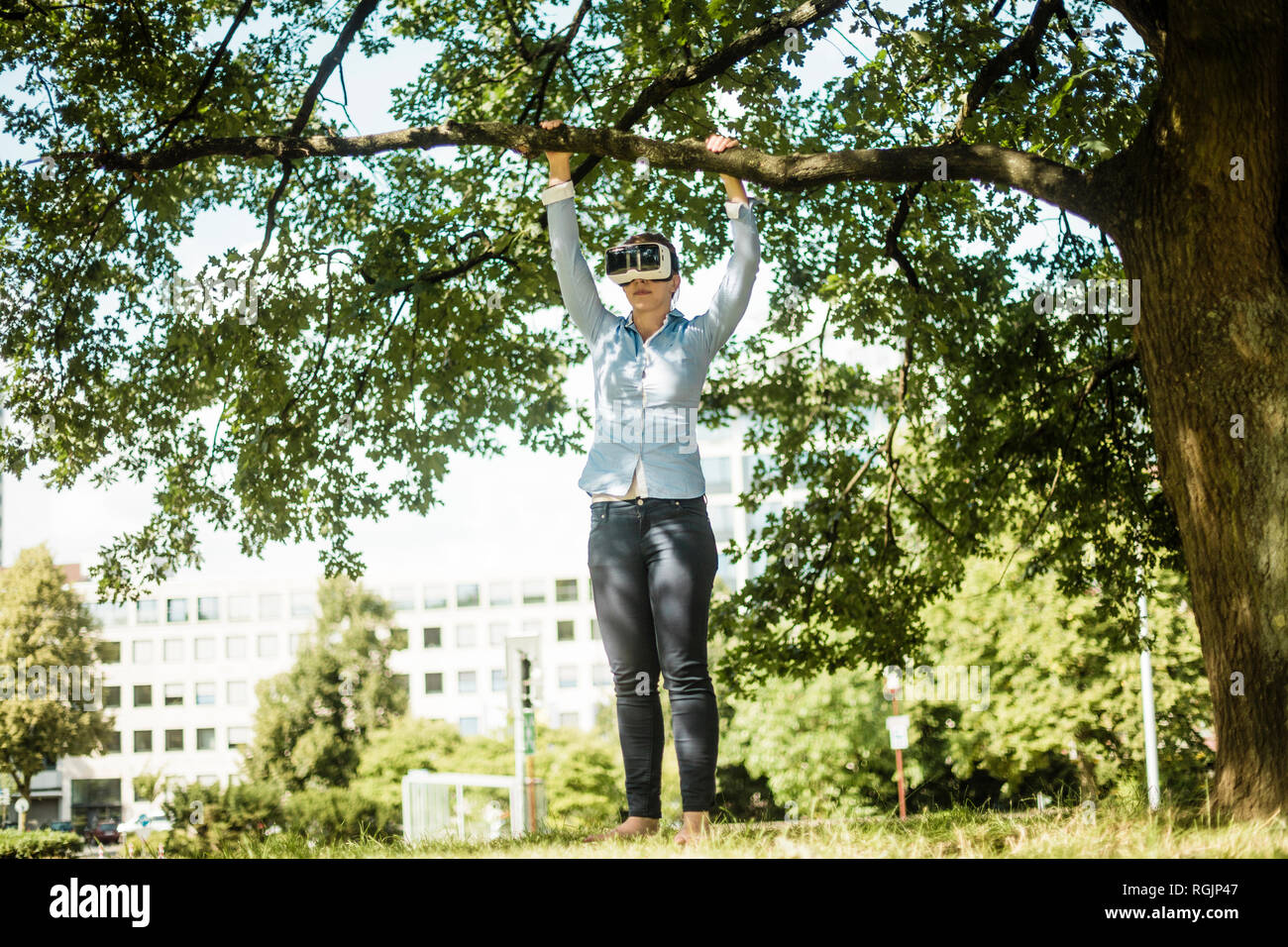 Woman in urban park at a tree wearing VR glasses Stock Photo