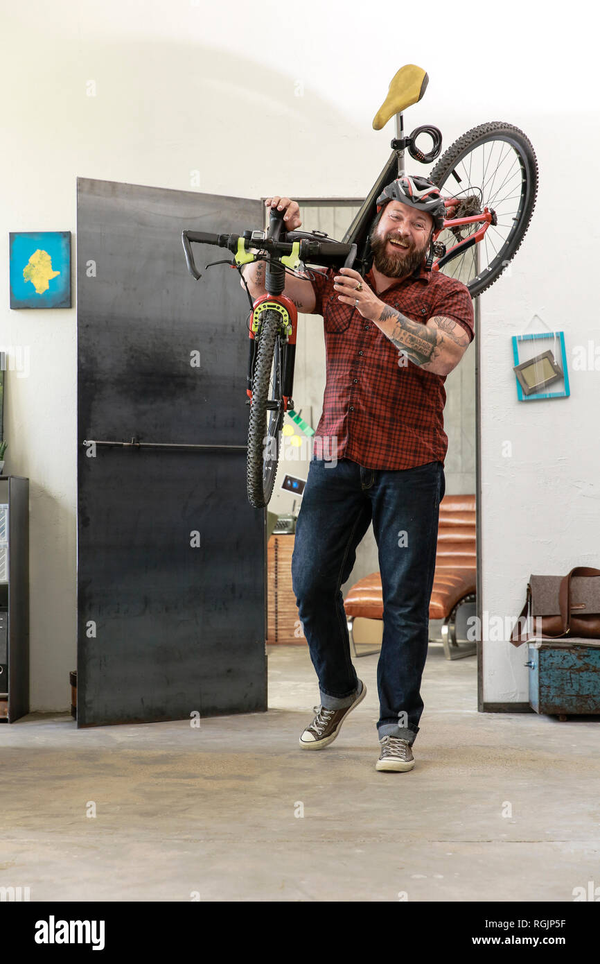 Portrait of laughing man carrying bicycle in office Stock Photo