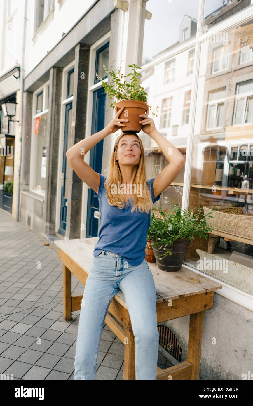 Netherlands, Maastricht, young woman balancing flowerpot on her head in the city Stock Photo