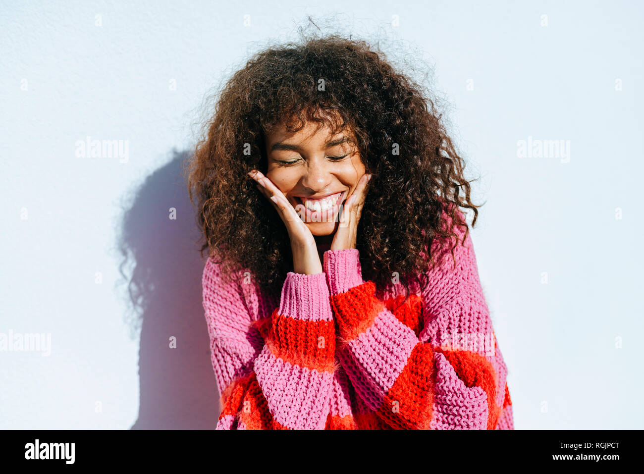 Portrait of laughing young woman with curly hair against white wall Stock Photo
