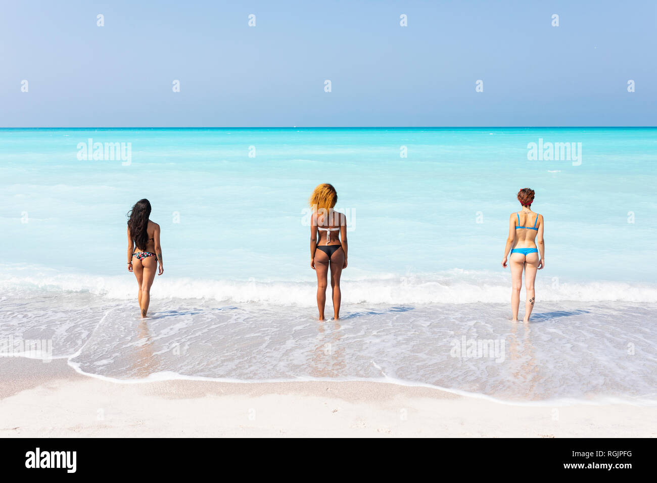 Young women standing at the sea, looking at distance, rear view Stock Photo