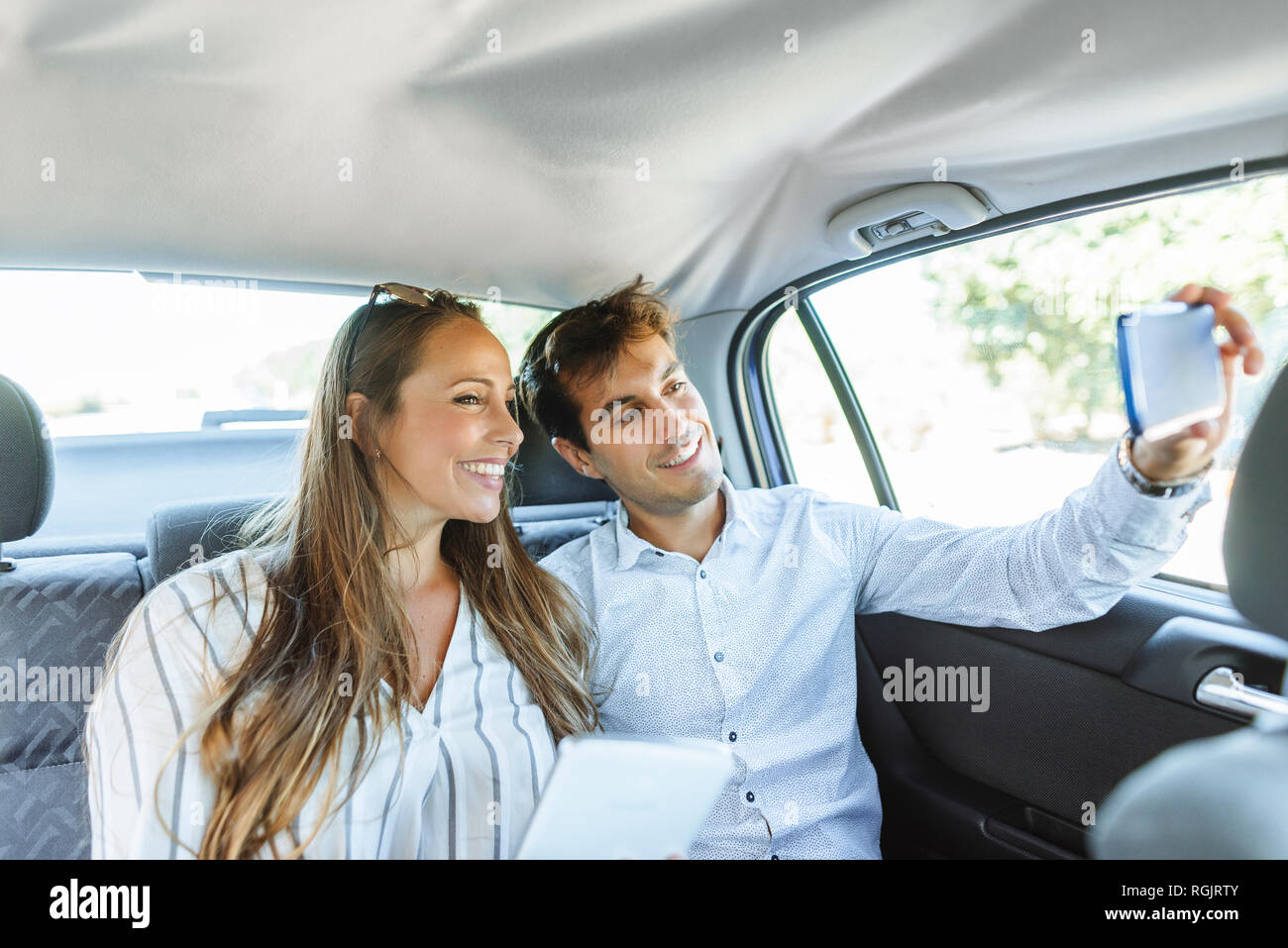 Smiling couple on back seat of a car taking a selfie Stock Photo