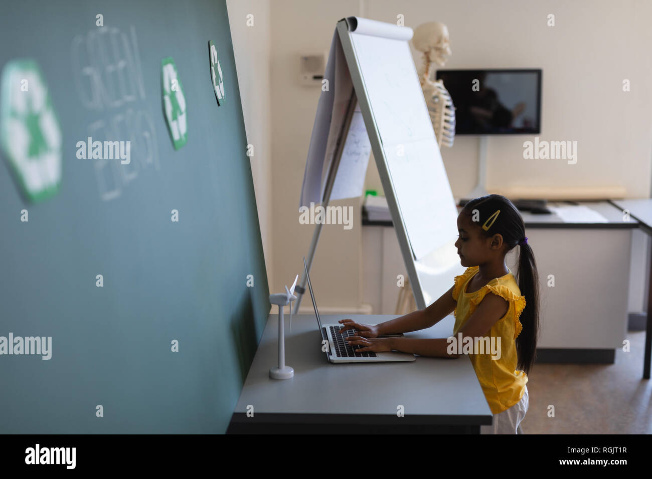 Side view of schoolgirl studying on laptop at desk in classroom of ...