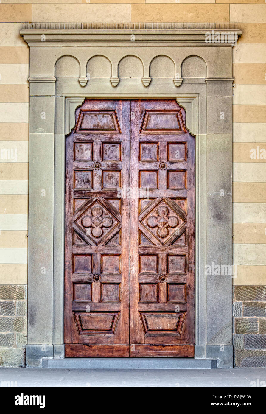 Photograph taken in the medieval village of Cortona in the heart of Tuscany. A weathered brown wood carved door has a hand carved stone frame. Stock Photo
