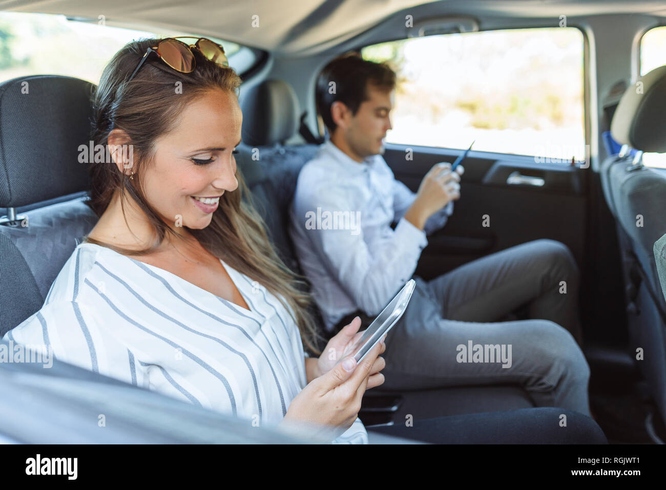 woman-man-using-tablet-cell-phone-back-seat-car-hi-res-stock