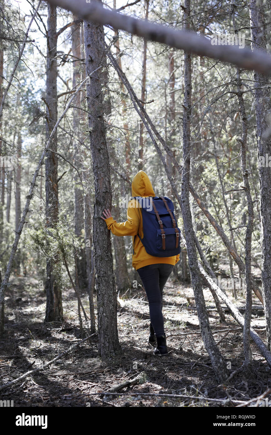 Rear view of young woman with yellow sweater and blue bag in the forest, exploring Stock Photo