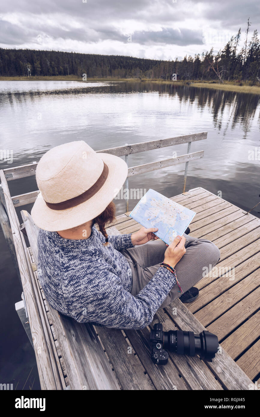 Sweden, Lapland, man with camera sitting on bench on a jetty looking at map Stock Photo