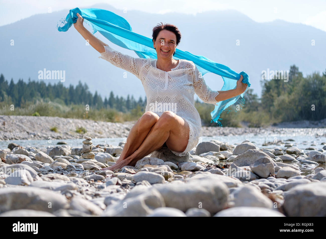 Happy woman holding swaying blue scarf at the riverside, Upper Bavaria, Germany Stock Photo