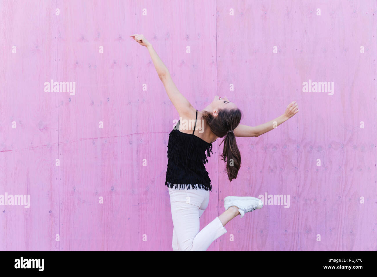 Happy young woman moving in front of pink wall Stock Photo