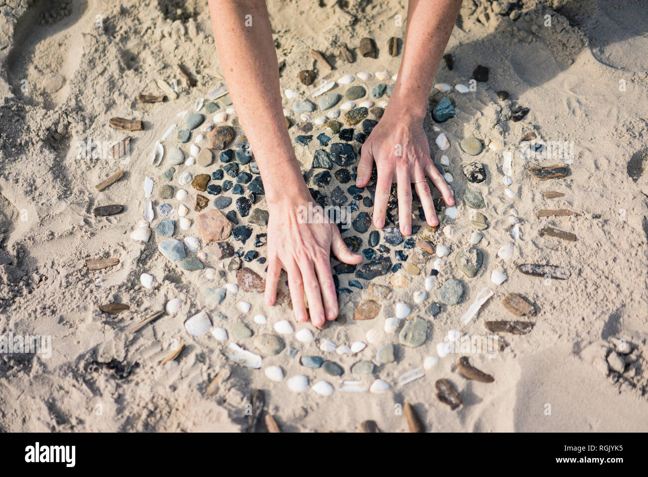 Mature woman making a heart from seashells on the beach Stock Photo