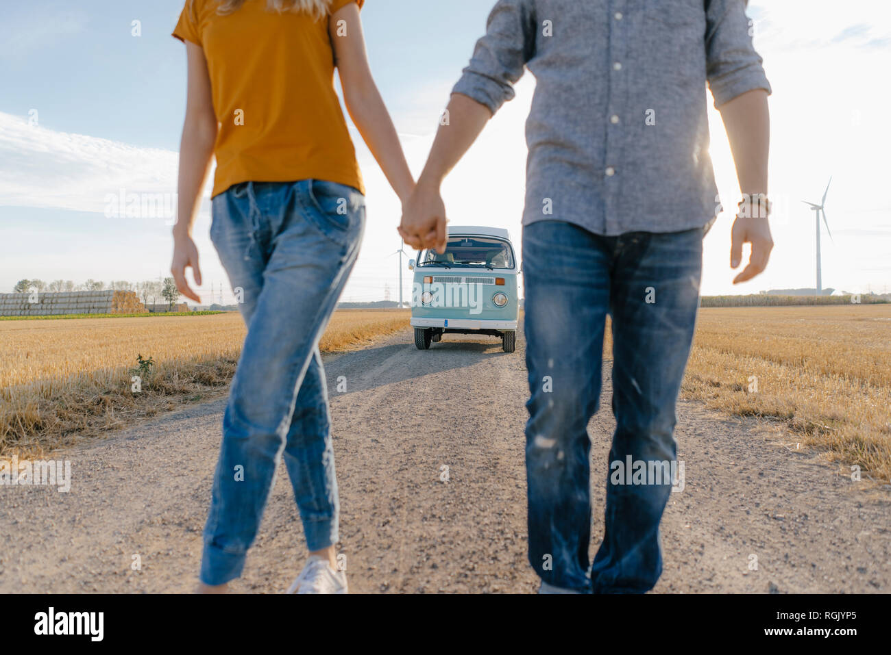 Close-up of couple walking on dirt track at camper van in rural landscape Stock Photo