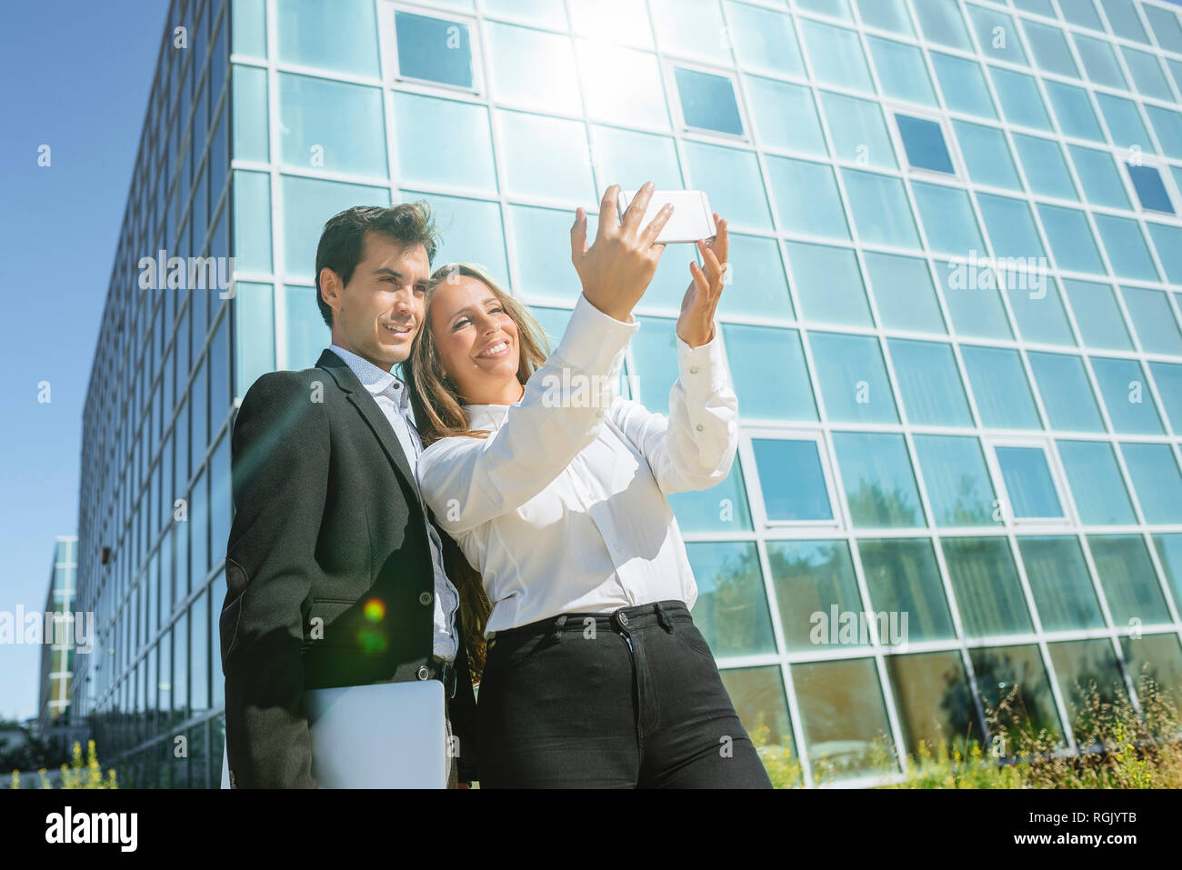 Smiling businesswoman and businessman taking a selfie outside office building Stock Photo