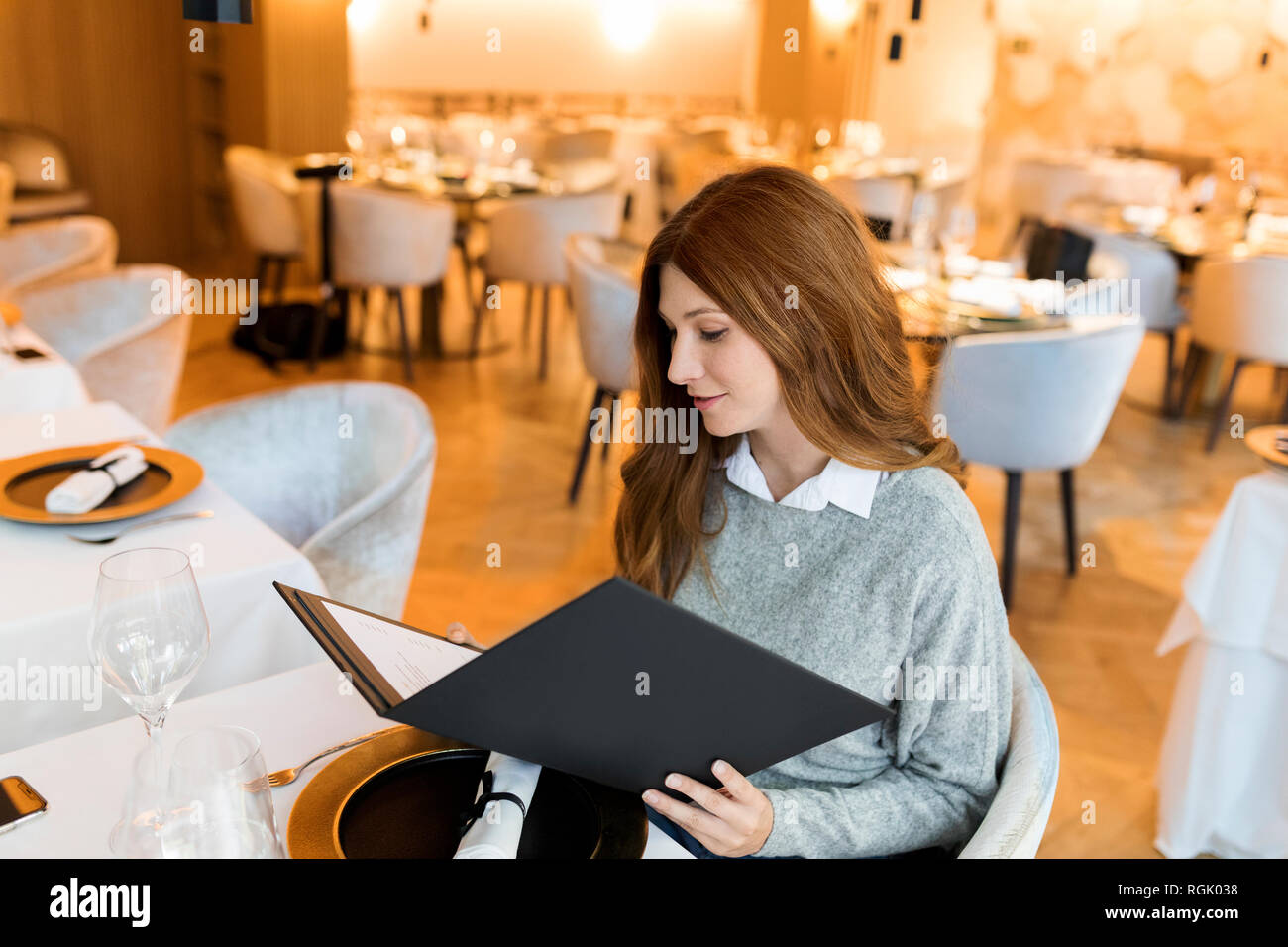 Woman sitting at table in a restaurant reading menu Stock Photo