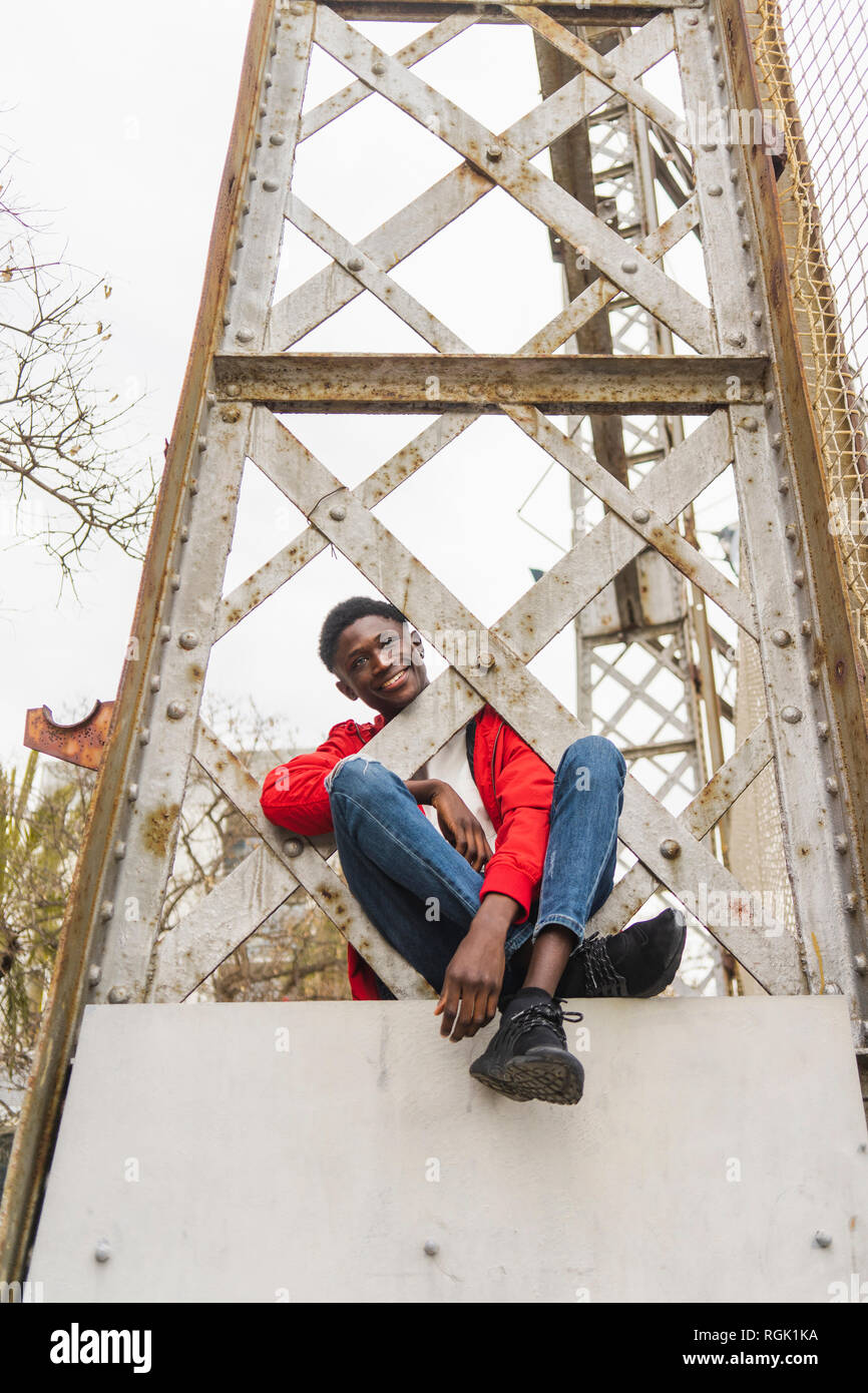 Young man sitting on pillar, smiling Stock Photo