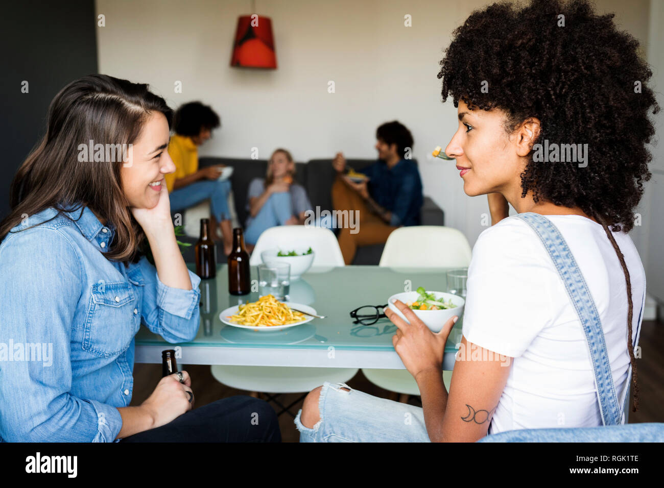 Girlfriends sitting at dining table with friends in background Stock Photo